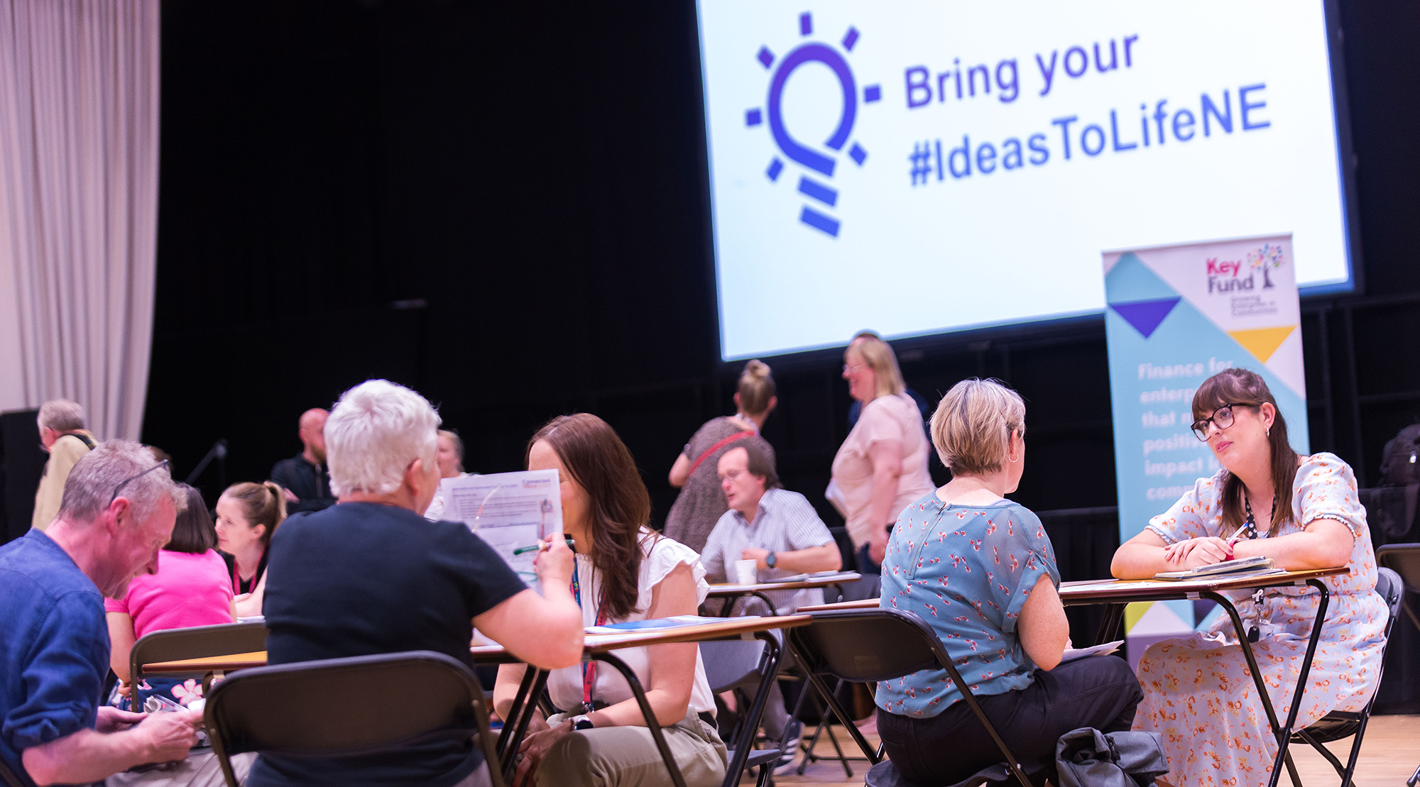 Tables of people talking in front of a screen saying Bring your Ideas to Life
